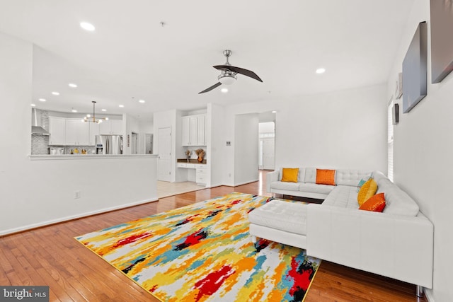 living room featuring recessed lighting, baseboards, ceiling fan with notable chandelier, and light wood-type flooring