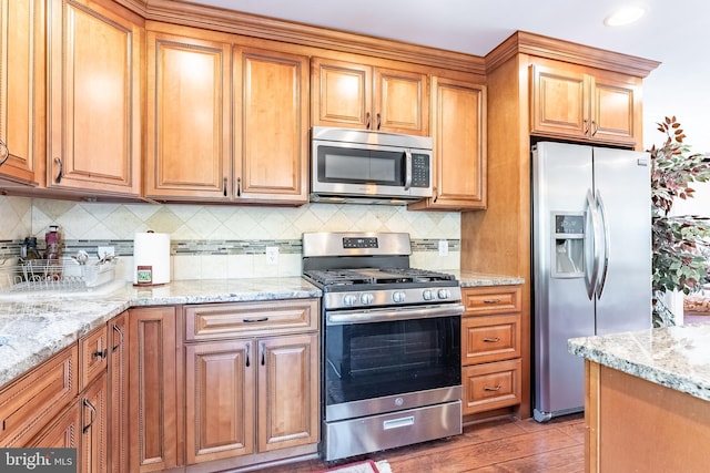 kitchen featuring backsplash, brown cabinets, light stone countertops, and appliances with stainless steel finishes