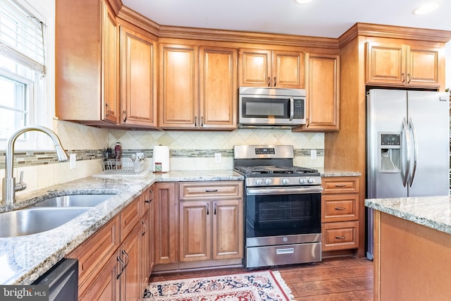 kitchen featuring appliances with stainless steel finishes, tasteful backsplash, a sink, light stone counters, and dark wood-type flooring