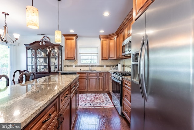 kitchen with appliances with stainless steel finishes, light stone counters, a sink, a chandelier, and brown cabinetry