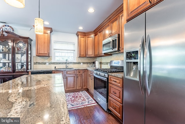kitchen featuring a sink, light stone counters, stainless steel appliances, and wood finished floors