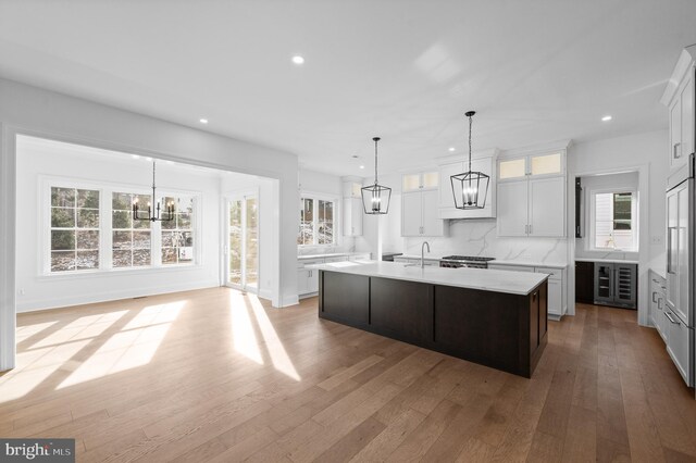 kitchen featuring a kitchen island with sink, light wood-type flooring, wine cooler, light countertops, and an inviting chandelier