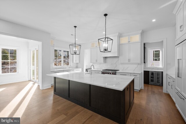 kitchen with a kitchen island with sink, a chandelier, recessed lighting, tasteful backsplash, and glass insert cabinets