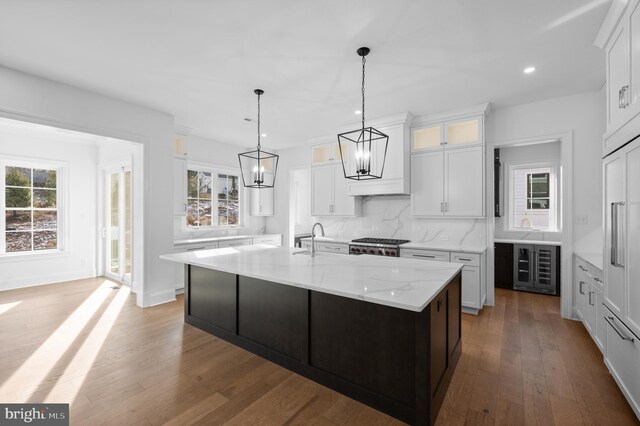 kitchen featuring tasteful backsplash, a chandelier, glass insert cabinets, recessed lighting, and an island with sink