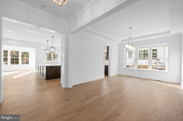 unfurnished living room with crown molding, light wood finished floors, a chandelier, baseboards, and a tray ceiling
