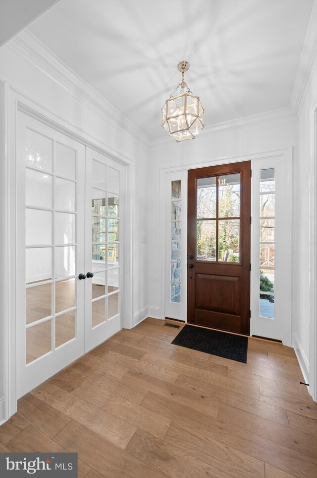 doorway to outside featuring a notable chandelier, ornamental molding, french doors, and light wood finished floors