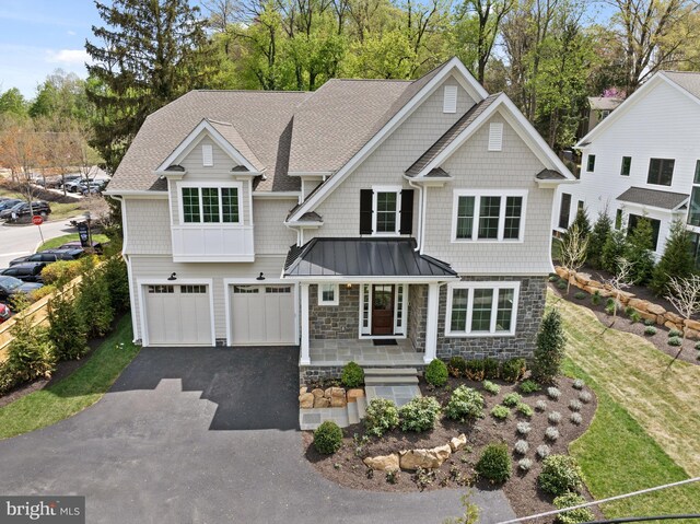 view of front of house featuring aphalt driveway, covered porch, stone siding, a standing seam roof, and an attached garage