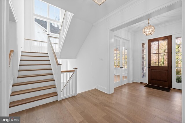 foyer featuring crown molding, wood finished floors, baseboards, a chandelier, and stairs