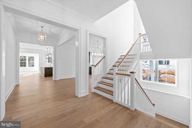 staircase featuring an inviting chandelier, baseboards, crown molding, and wood finished floors