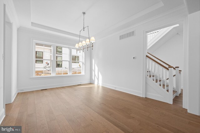unfurnished dining area with a raised ceiling, stairs, a chandelier, and hardwood / wood-style floors