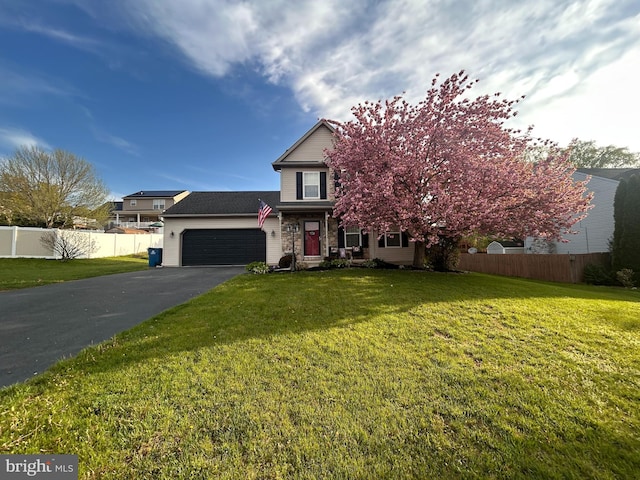 traditional-style house featuring an attached garage, a front lawn, aphalt driveway, and fence