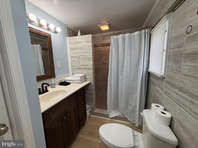 bathroom featuring vanity, wood finished floors, toilet, tile walls, and a tile shower