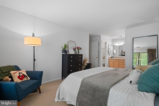 bedroom with baseboards, connected bathroom, and light carpet