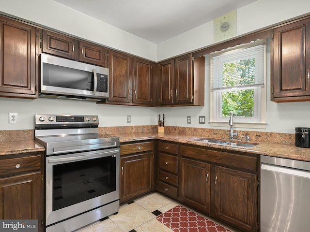 kitchen with stainless steel appliances, light tile patterned floors, a sink, and dark brown cabinets