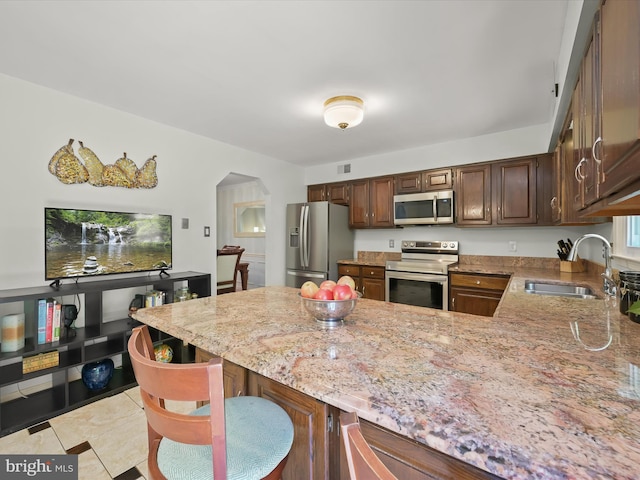 kitchen featuring a sink, appliances with stainless steel finishes, light stone countertops, and arched walkways