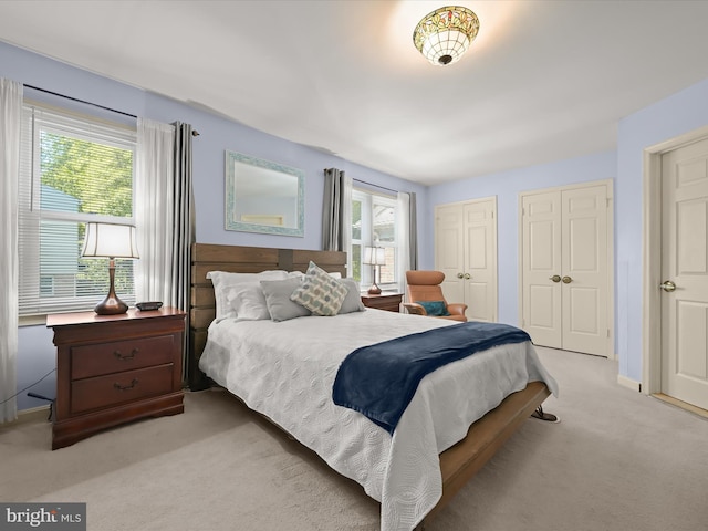 bedroom with baseboards, multiple closets, and light carpet