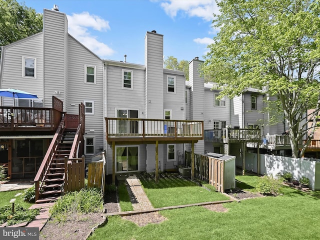 rear view of house featuring a chimney, a lawn, a deck, stairway, and fence