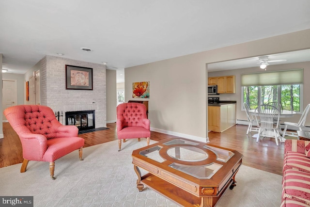 living area featuring a brick fireplace, a ceiling fan, light wood finished floors, and a baseboard radiator