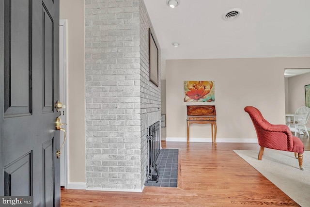 interior space with visible vents, light wood-style flooring, a brick fireplace, and baseboards