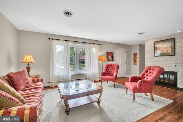 living area with visible vents, a brick fireplace, wood finished floors, and baseboard heating
