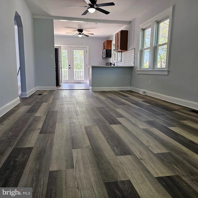 unfurnished living room with visible vents, dark wood-style flooring, baseboards, ceiling fan, and arched walkways