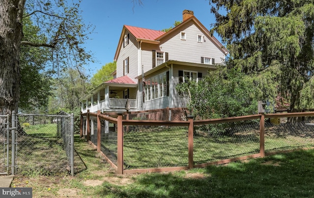 back of property with metal roof, a chimney, fence private yard, a gate, and a yard