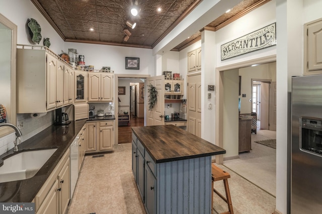 kitchen featuring a sink, a kitchen breakfast bar, butcher block countertops, stainless steel refrigerator with ice dispenser, and ornamental molding