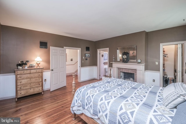 bedroom with a brick fireplace, a wainscoted wall, a spacious closet, and hardwood / wood-style floors