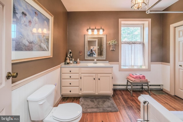 bathroom with a wainscoted wall, baseboard heating, toilet, and wood finished floors