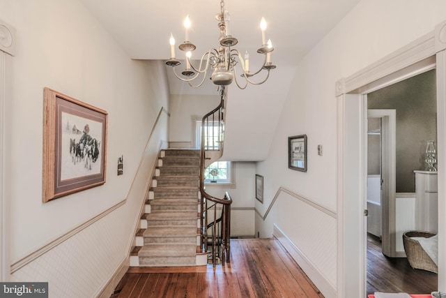 staircase with a notable chandelier, wainscoting, and hardwood / wood-style flooring