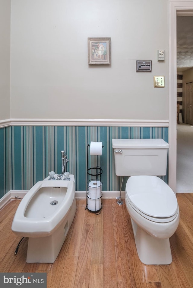 bathroom with wainscoting, toilet, wallpapered walls, and a bidet