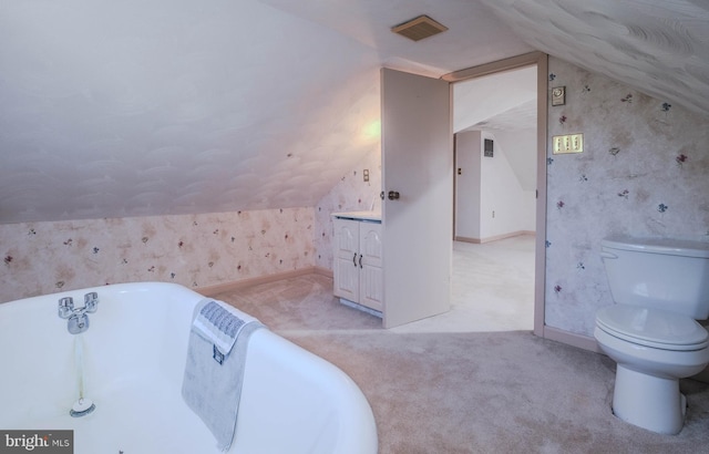 bathroom with visible vents, toilet, wallpapered walls, a freestanding bath, and vaulted ceiling