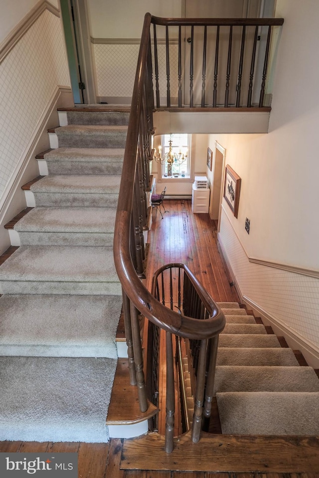 staircase with wallpapered walls, an inviting chandelier, a wainscoted wall, and hardwood / wood-style floors