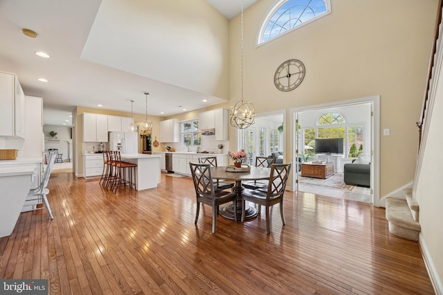 dining space featuring a high ceiling, a notable chandelier, baseboards, and light wood-type flooring