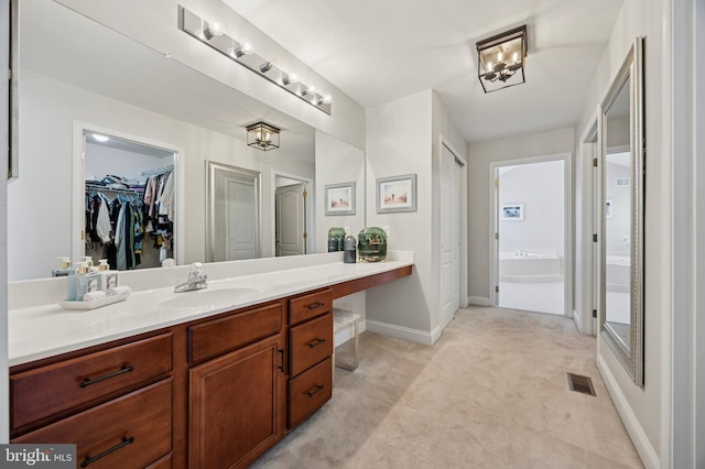 bathroom with visible vents, vanity, baseboards, a bath, and a spacious closet