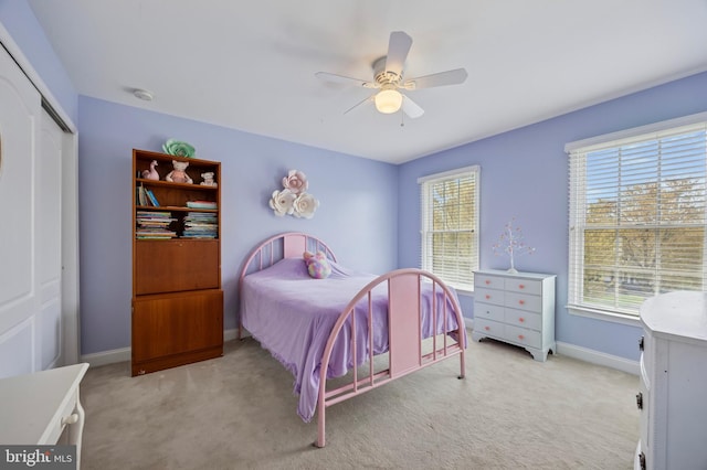 bedroom with baseboards, ceiling fan, a closet, and light colored carpet