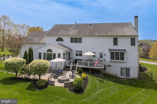 rear view of property featuring a yard, a deck, a chimney, and an outdoor fire pit