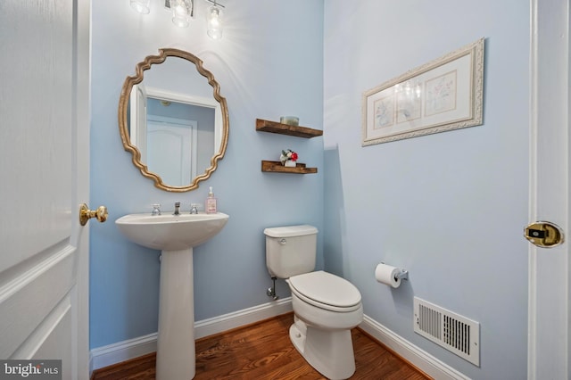 bathroom with a sink, toilet, baseboards, wood finished floors, and visible vents