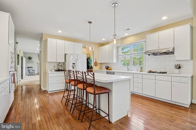 kitchen with light wood-style floors, white appliances, a kitchen breakfast bar, range hood, and visible vents