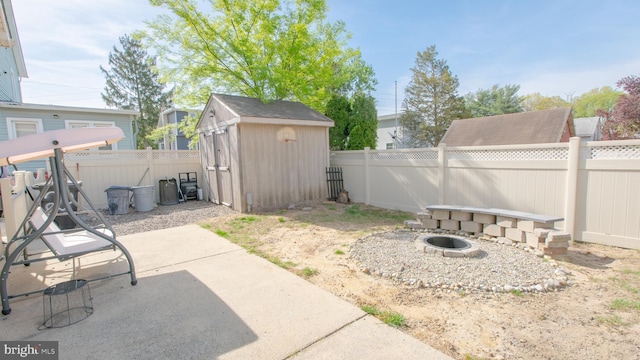 view of yard featuring a storage unit, a fenced backyard, a patio area, an outdoor structure, and a fire pit
