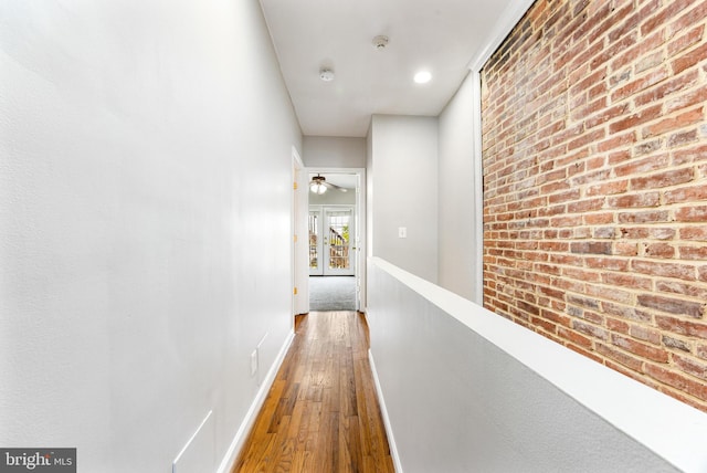 hall with baseboards, wood-type flooring, and brick wall