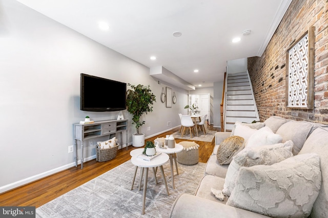 living area featuring brick wall, stairs, recessed lighting, baseboards, and wood finished floors