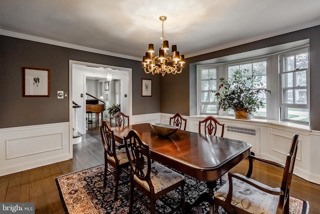 dining area with a wainscoted wall, a notable chandelier, ornamental molding, a decorative wall, and dark wood-type flooring