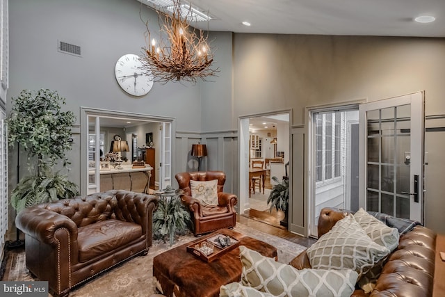 living room with visible vents, a towering ceiling, wood finished floors, and an inviting chandelier