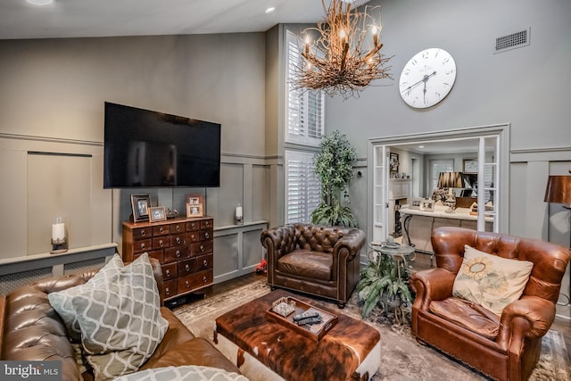 living room featuring visible vents, an inviting chandelier, wood finished floors, a decorative wall, and a high ceiling