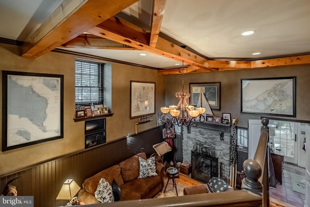 living area featuring a stone fireplace, a wainscoted wall, beamed ceiling, a notable chandelier, and recessed lighting
