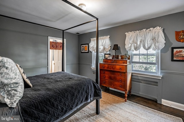 bedroom with baseboards, visible vents, wood finished floors, and radiator