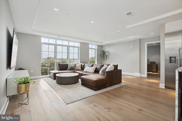 living room with visible vents, baseboards, recessed lighting, a raised ceiling, and light wood finished floors