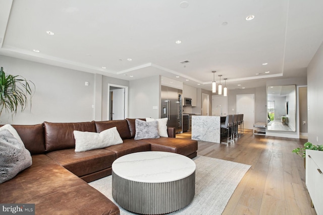 living room with recessed lighting, light wood-style flooring, and a raised ceiling