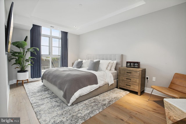 bedroom with baseboards, a tray ceiling, light wood-type flooring, and visible vents